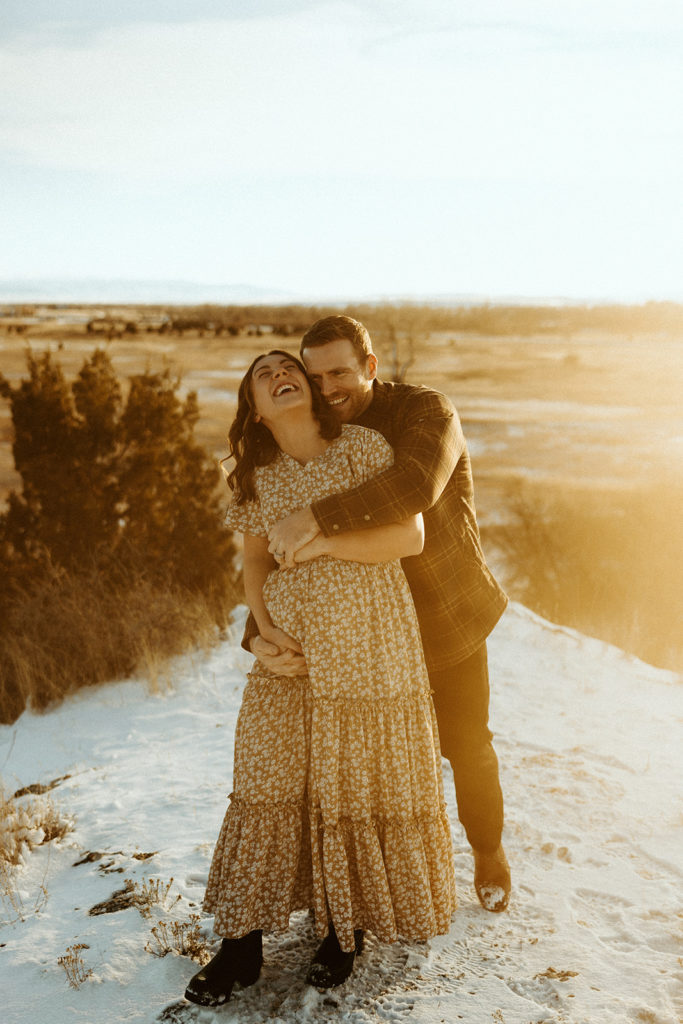 Man and woman standing in a Montana field and posing for maternity photos