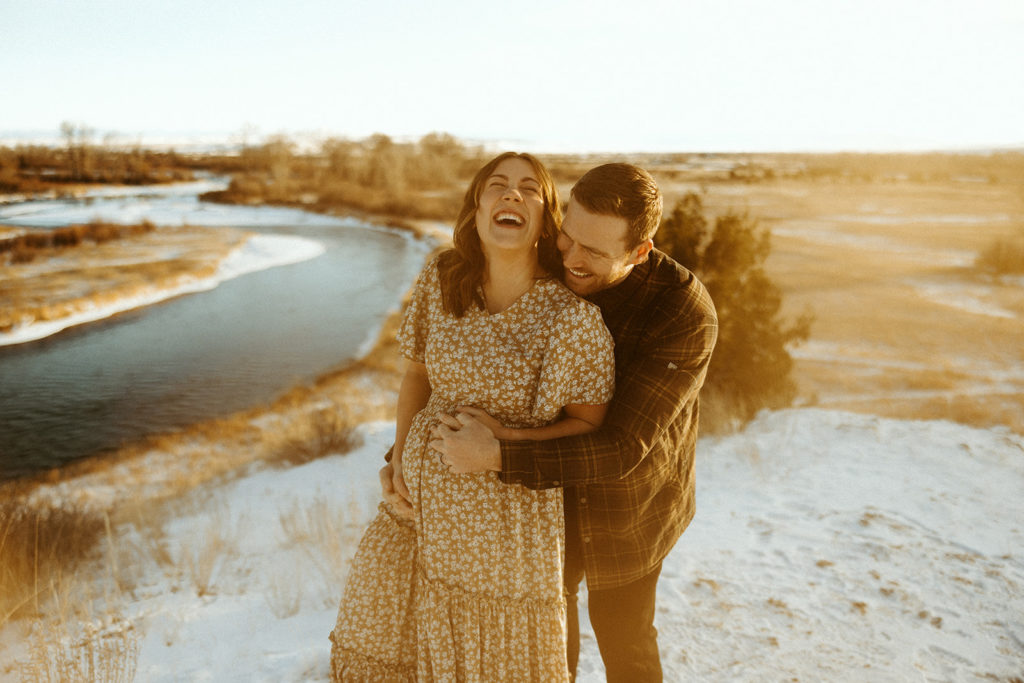 Couple lauging and posing for winter maternity photos in Montana